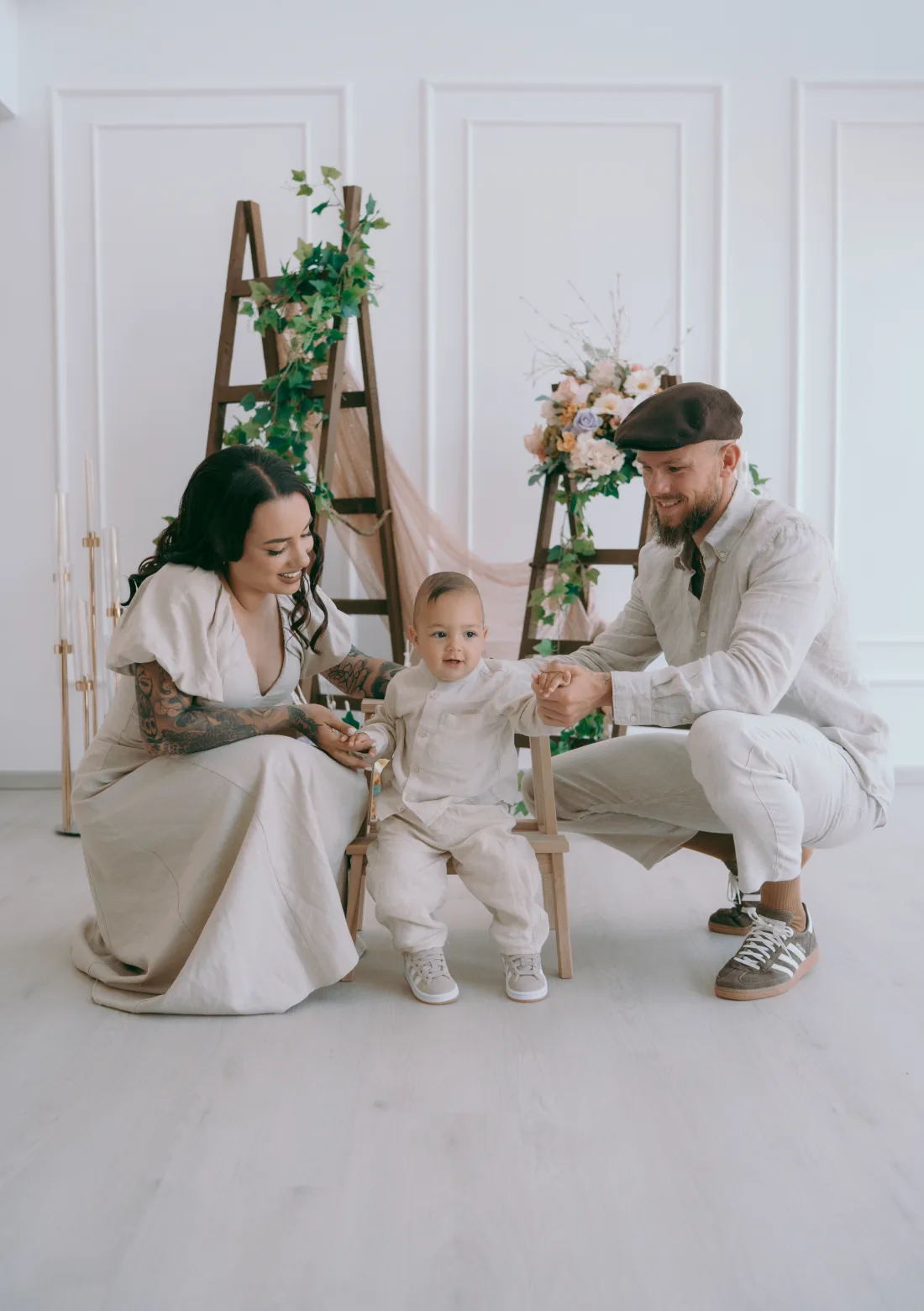 Naomi and Jonny Crawford holding their son Theodoros's hands as he sits between them, all wearing neutral linen.