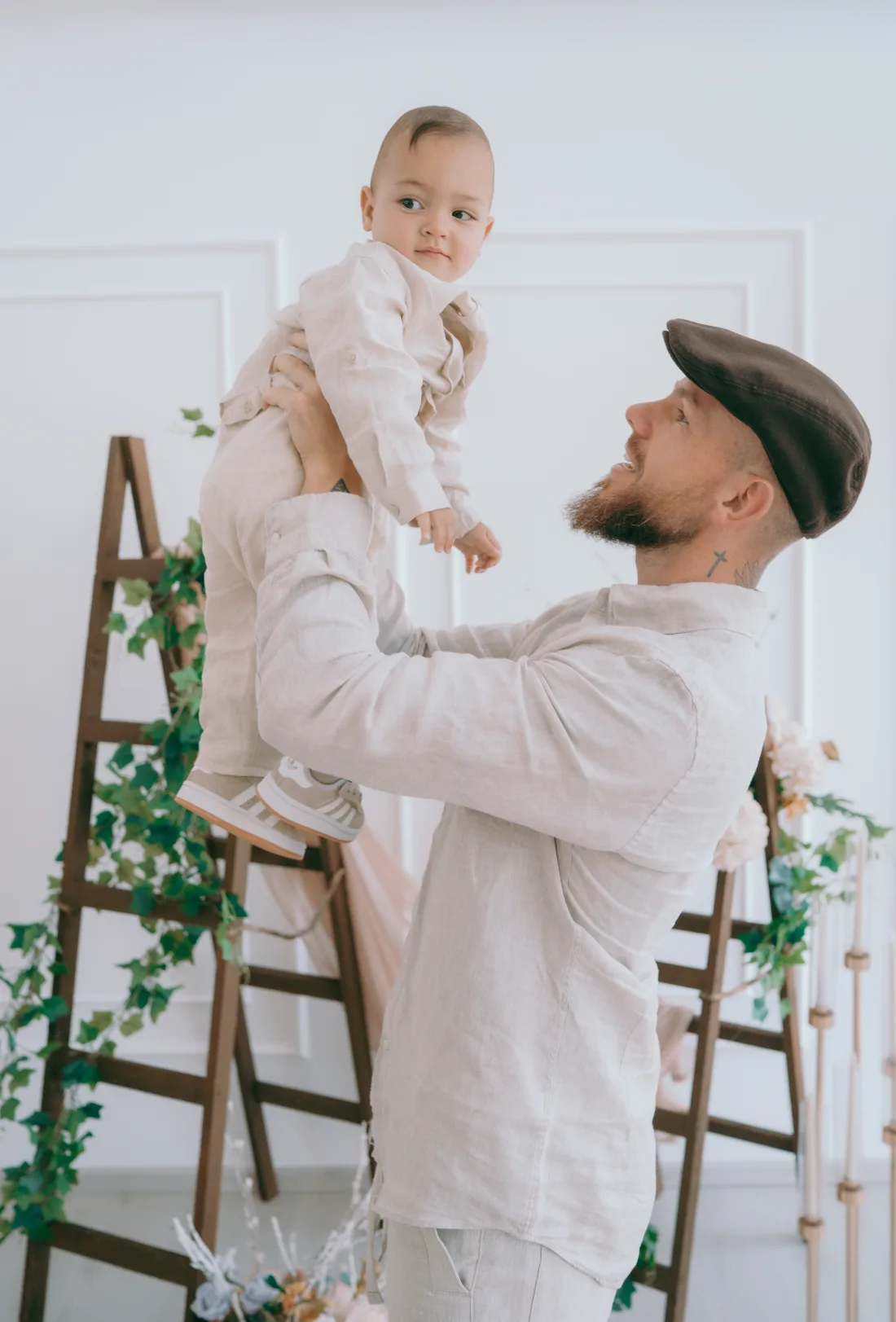 Jonny Crawford lifting his son Theodoros, both dressed in light linen.