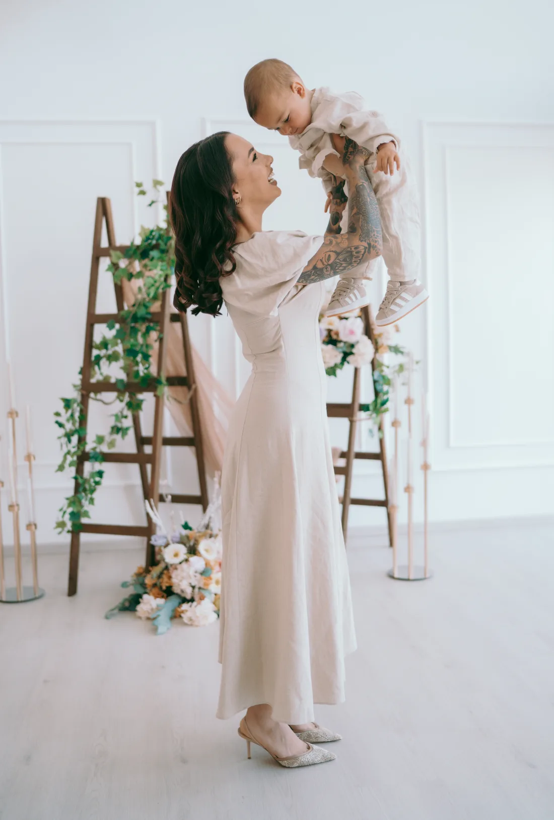 Naomi Crawford lifting her son Theodoros, both dressed in pale linen.